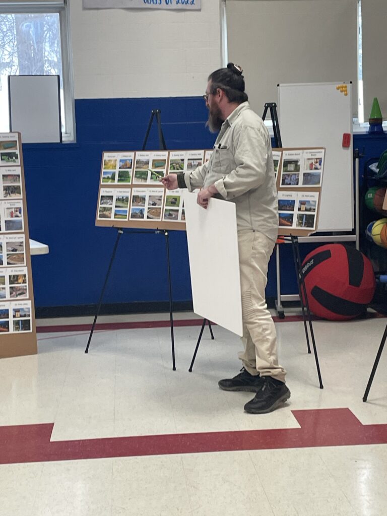 RDG team member Nate Card stands before an easel-mounted display board of labeled reference photographs, presenting design options to workshop participants.